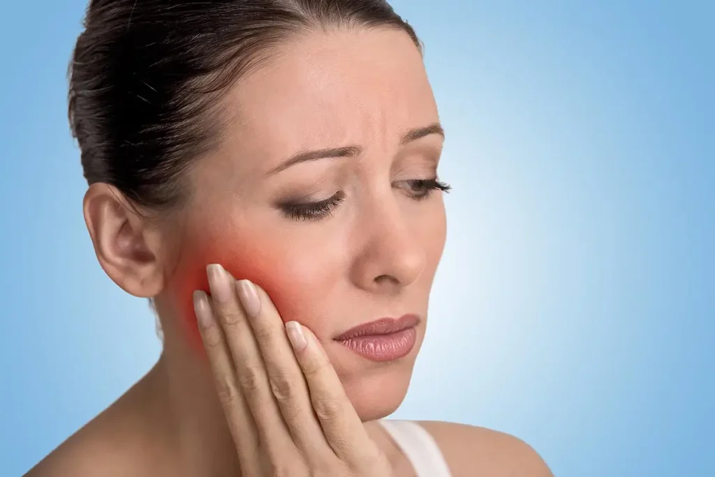 Woman holding cheek while experiencing tooth pain.