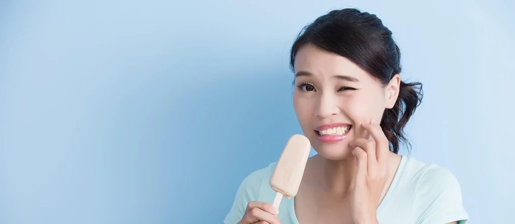 Person having tooth pain from sensitive teeth while holding an ice cream