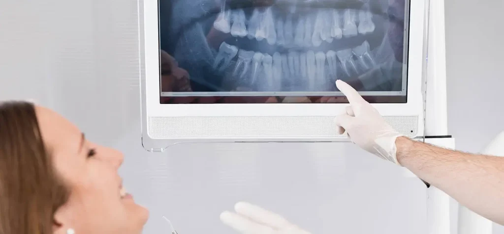 Dentist pointing to teeth x-ray in front of smiling patient.